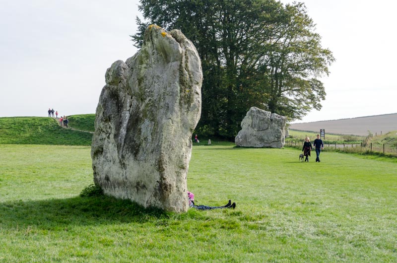 Ein Frau lehnt an einen großen Stein im Steinkreis von Avebury in England