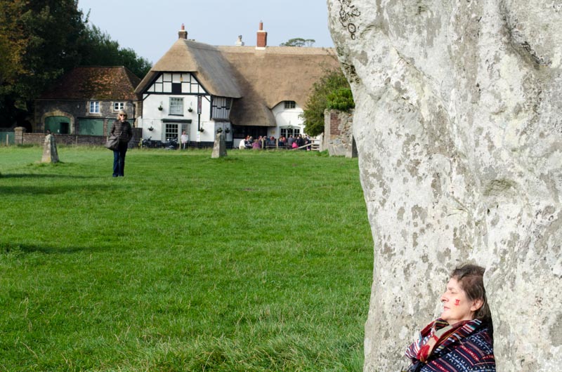 Ein Frau lehnt an einen großen Stein im Steinkreis von Avebury in England. 